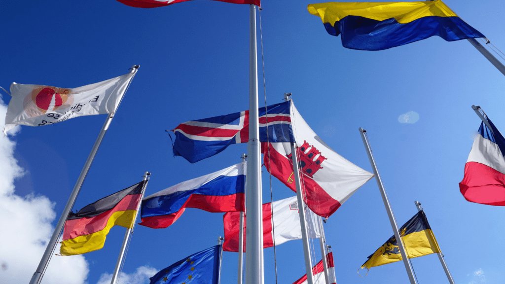 many flags are flying in the wind against a blue sky